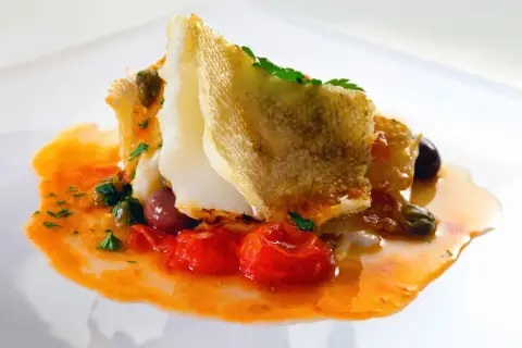 Delicioso bacalao encebollado con tomates, aceitunas y alcaparras en una salsa naranja vibrante.