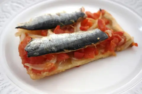 Rebanada de masa con tomate, cebolla y dos sardinas enteras, un plato que recuerda a las sardinas San Juan.