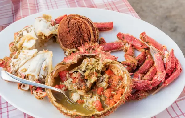 Centollo marisco preparado en una fuente blanca, con su coral y patas rojas. Una cuchara sirve el interior jugoso.